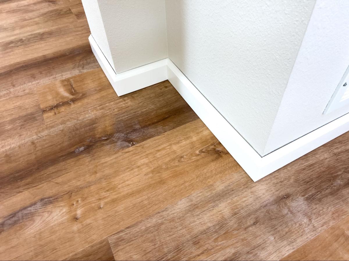 Strakke afwerking van een vinylvloer met witte plinten langs de muur.
